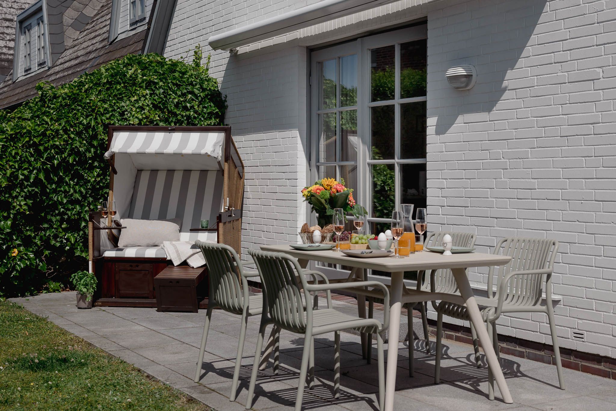 Strandkorb und gedeckter Gartentisch einer Ferienwohnung auf Sylt